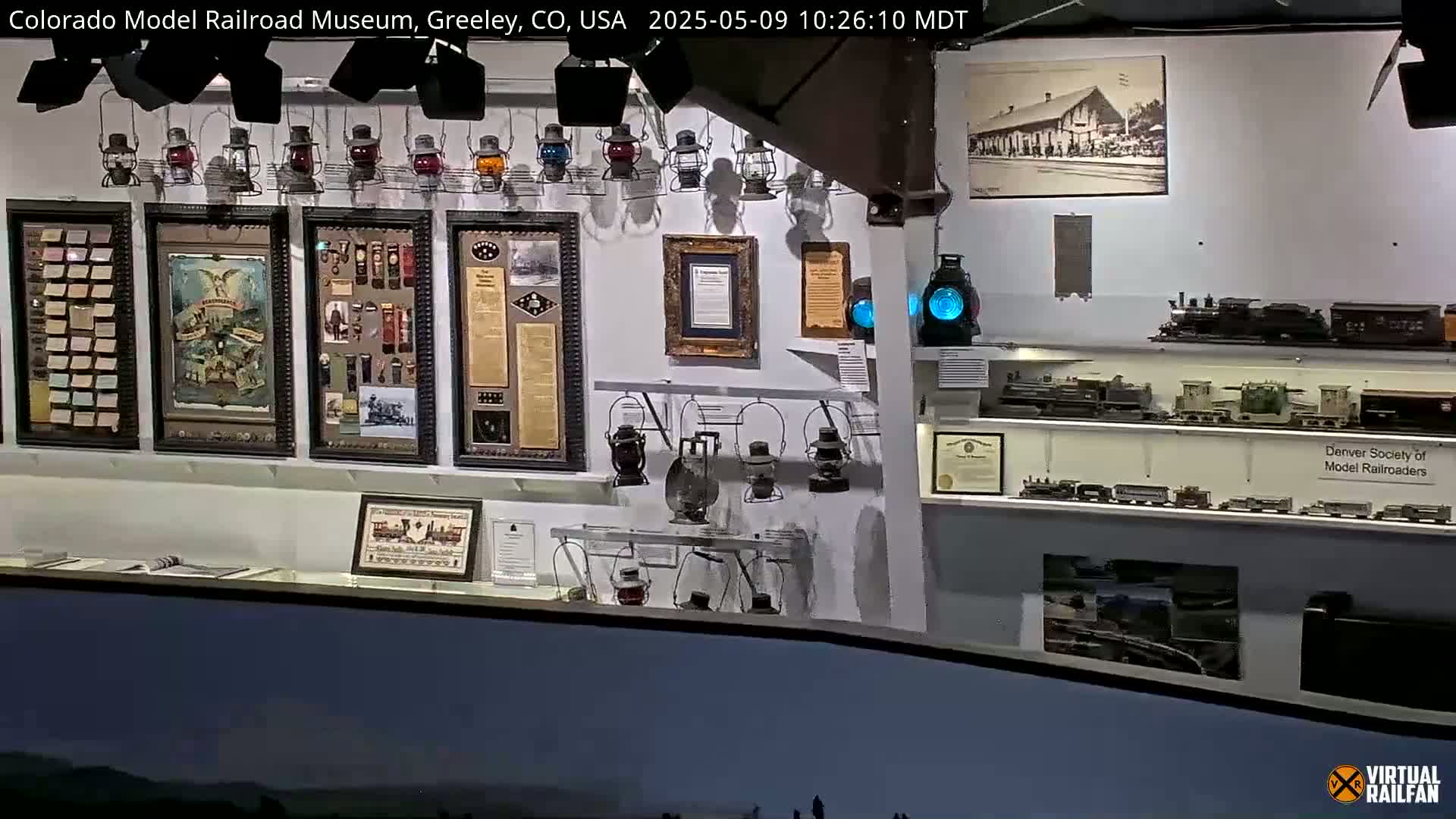 An indoor museum display showcases various railroad artifacts, including framed pictures, lanterns, and model trains.