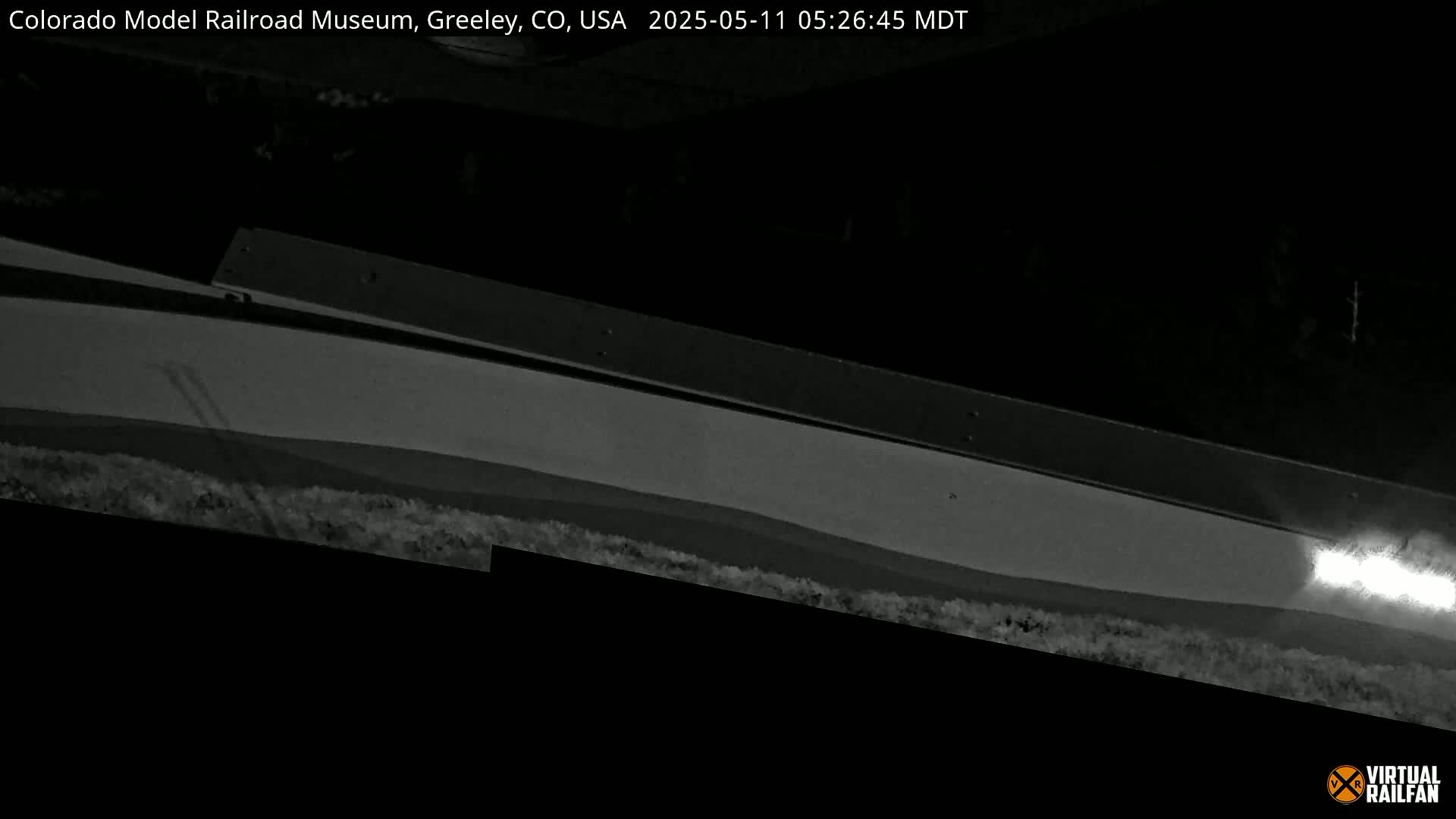 A low-angle, nighttime, grayscale view shows a long, flat, slightly angled surface with a bright light source visible at the lower right edge.