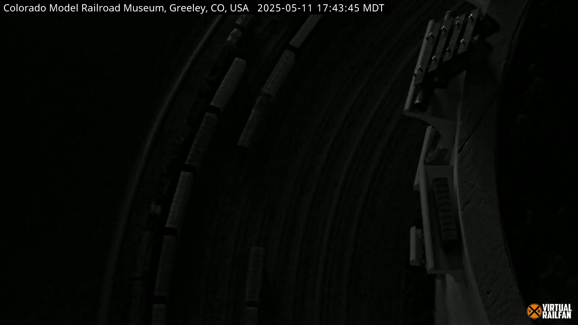 A dark, nighttime view of a model train track with a train moving along a curved section.
