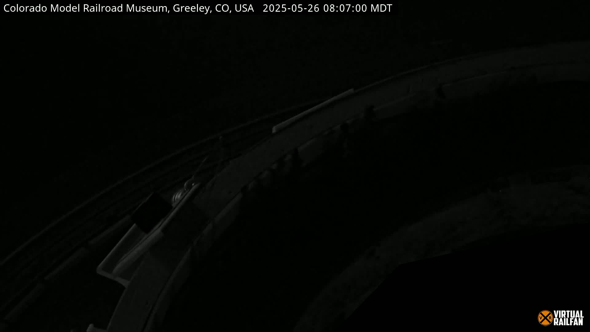 A dark, nighttime image shows a section of curved model train track.