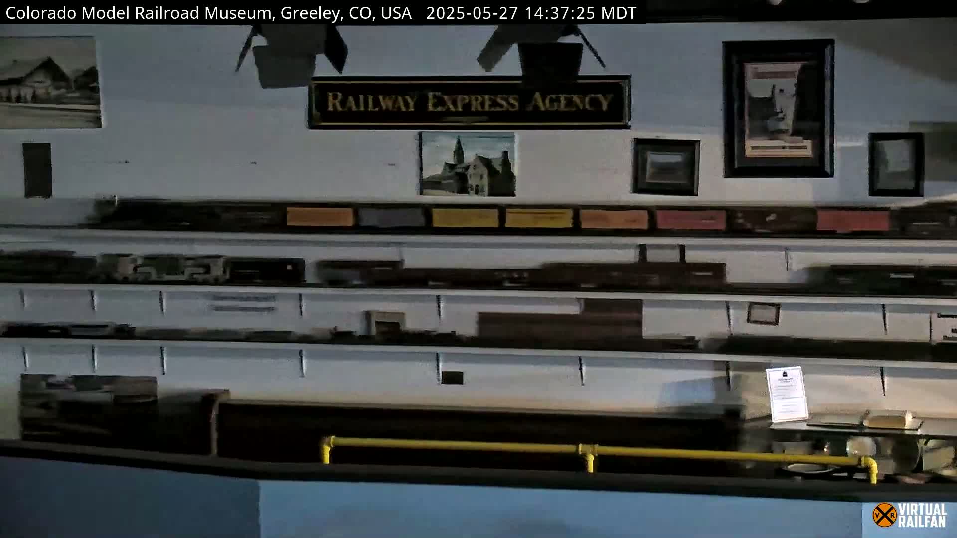 A museum display case filled with model trains and railway-themed pictures and artifacts is shown indoors.