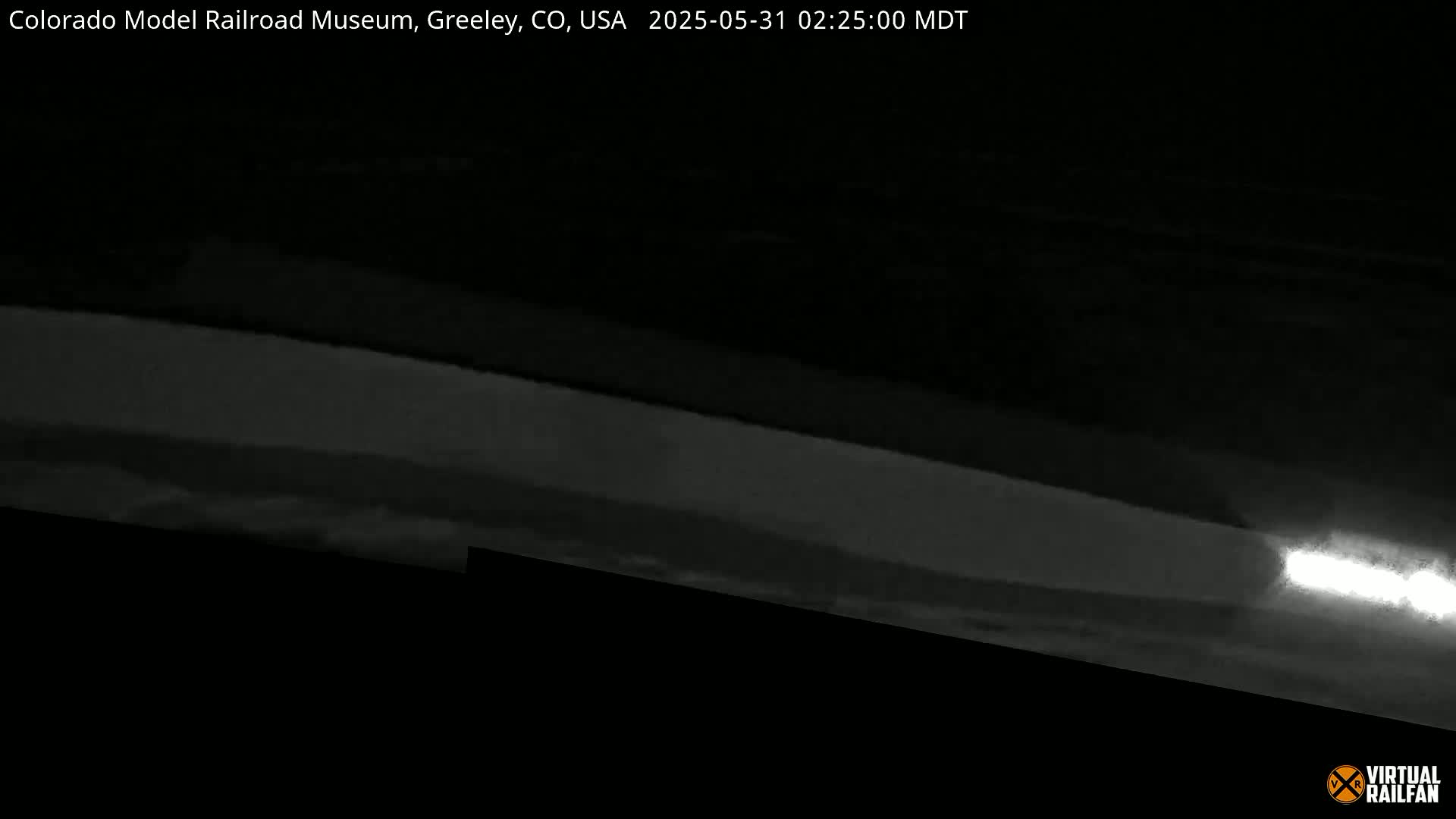 A low-light, nighttime image shows a brightly lit area at the bottom right, possibly a headlight, appearing to be on a dark road or track.