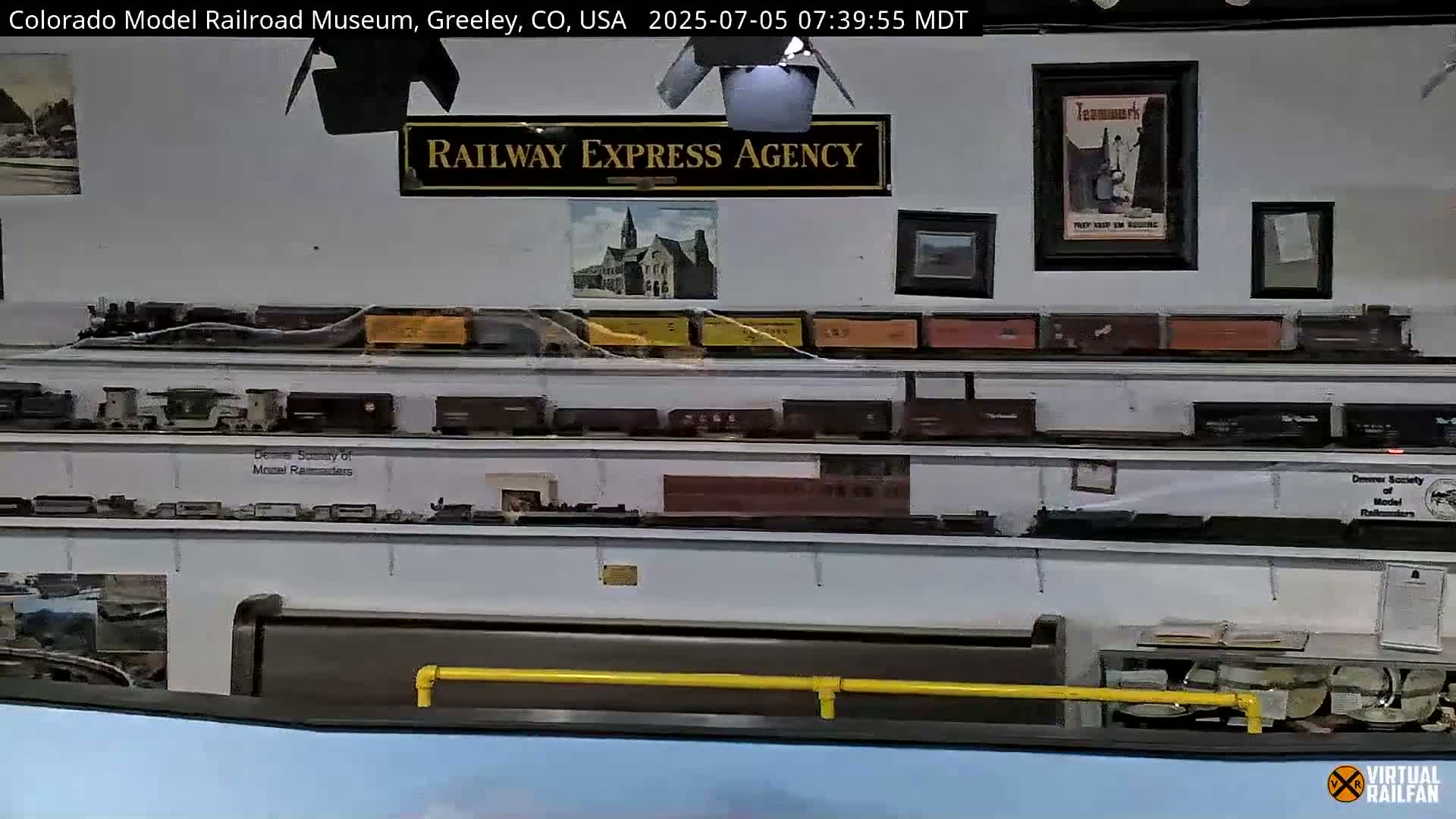 An indoor display of model trains and railroad memorabilia on shelves is visible, with framed pictures and a sign reading "Railway Express Agency" on the wall.