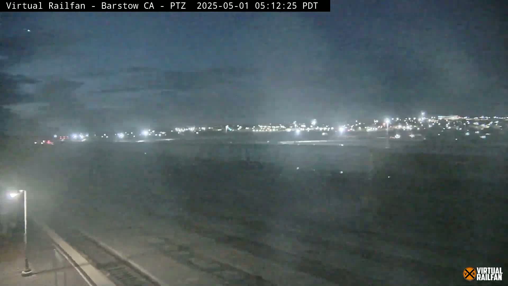 A nighttime view shows a flat, hazy landscape with a distant city illuminated by lights under a dark sky.