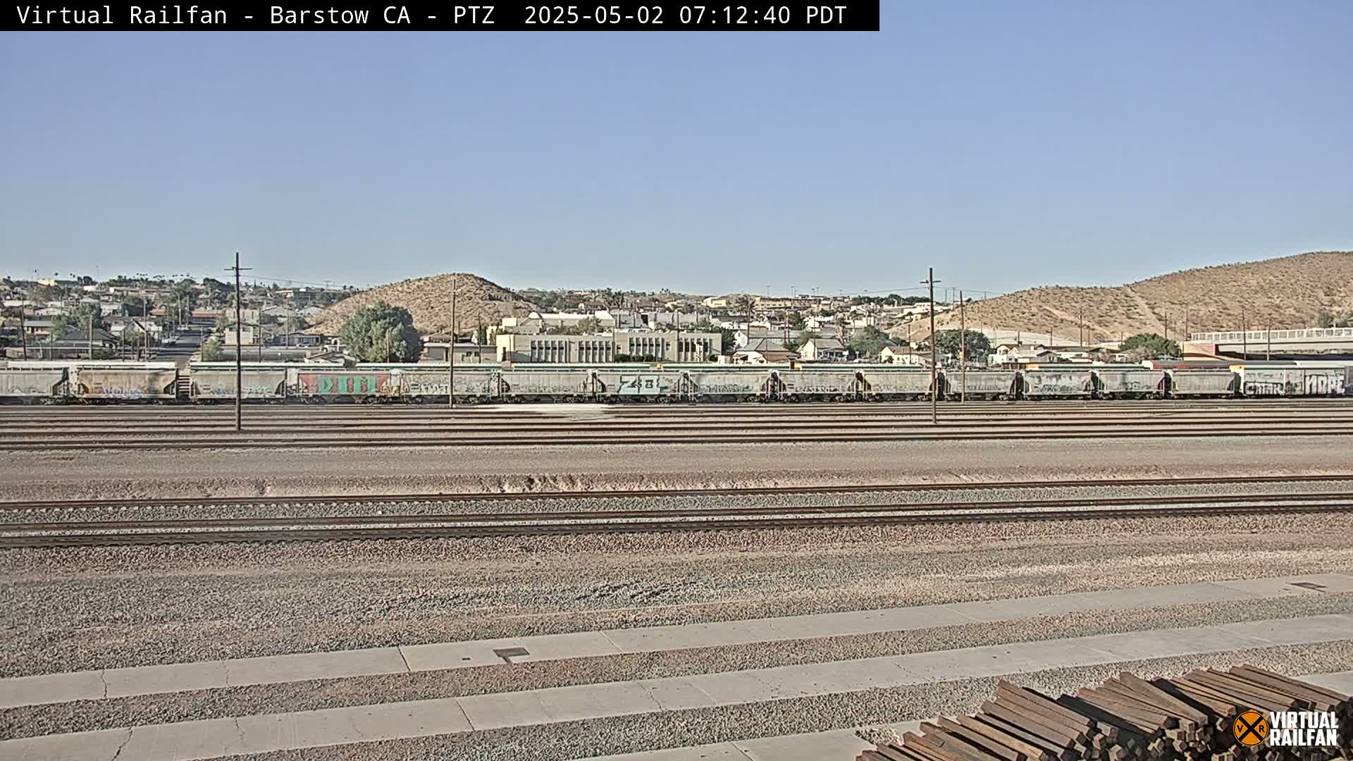 A long line of graffiti-covered train cars sits on parallel train tracks under a clear sky in a desert town.