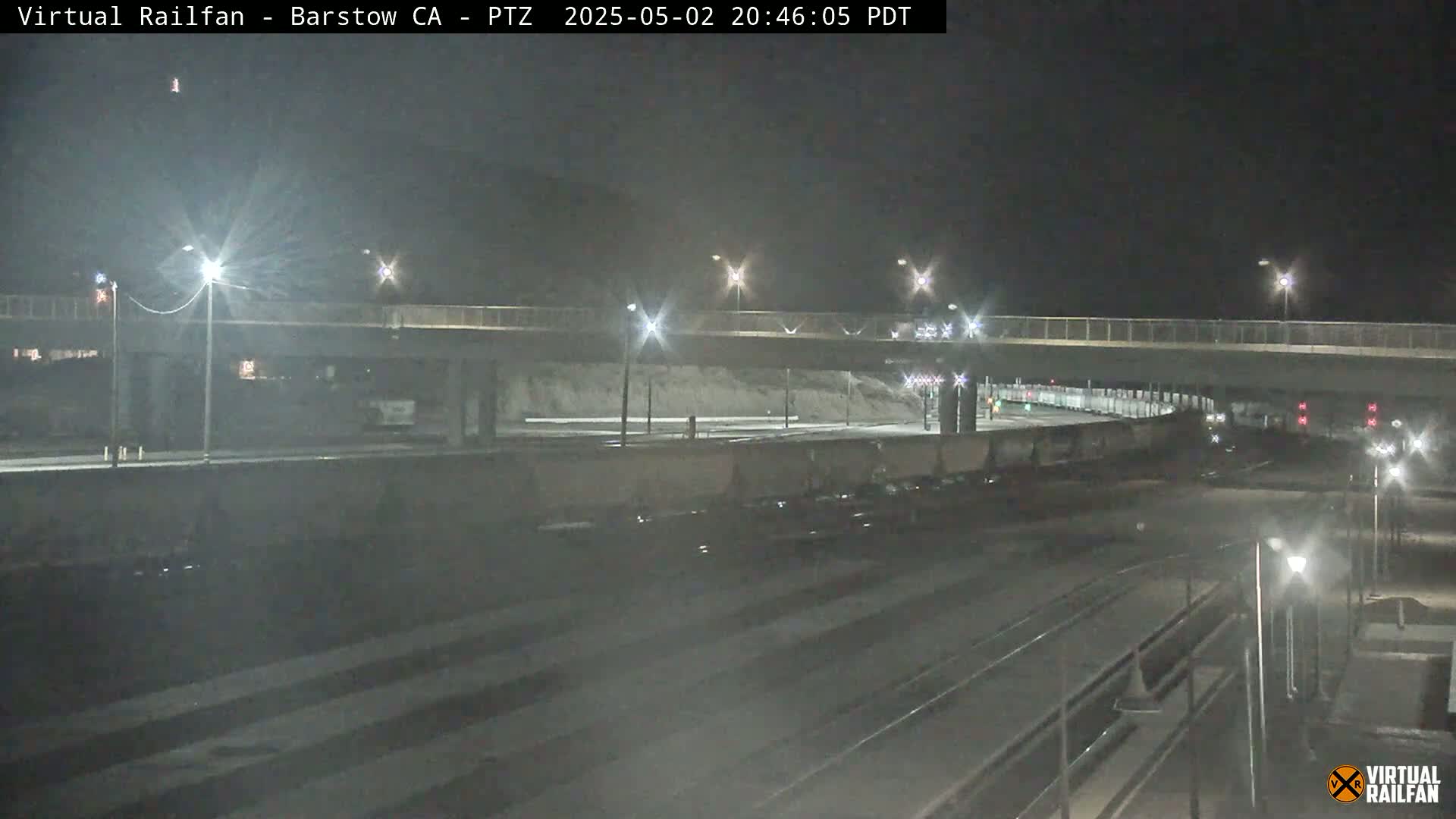 A nighttime view of a highway overpass and railroad tracks, with several cars parked below the overpass.