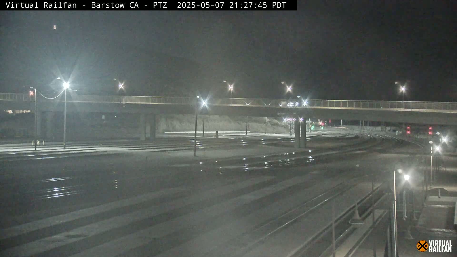 A nighttime view of a snow-dusted rail yard with a road overpass, illuminated by streetlights.