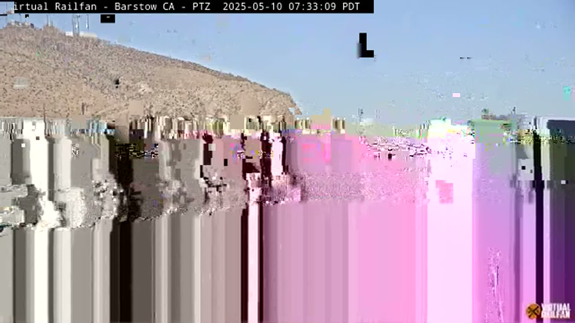 A mostly clear day reveals a tan, hilly landscape with a heavily pixelated foreground.