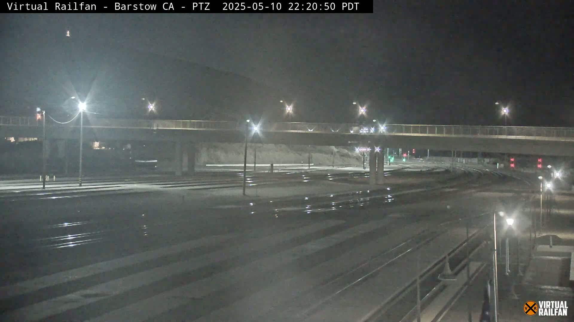 A nighttime view of a railway crossing under a bridge, lightly dusted with snow.