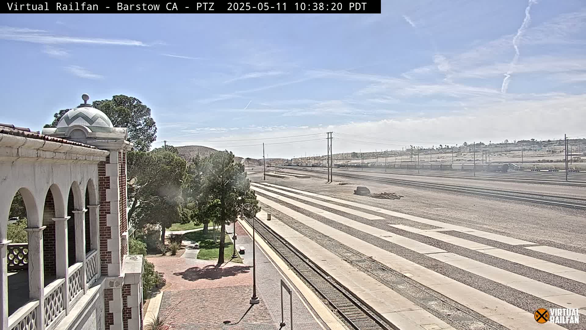 A view of train tracks extending into the distance under a mostly clear sky, alongside a building with arched walkways and a domed roof.