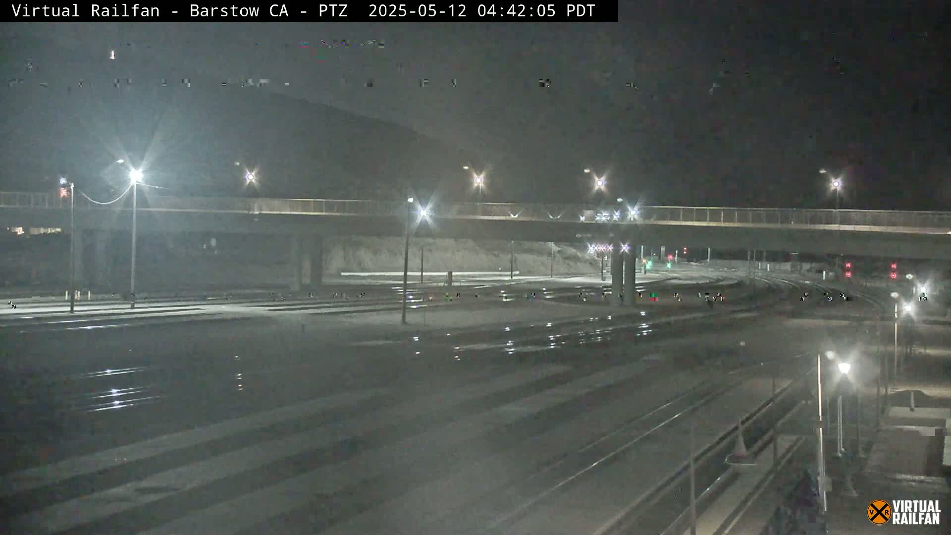 A nighttime view of a mostly empty rail yard with a roadway overpass, illuminated by streetlights.