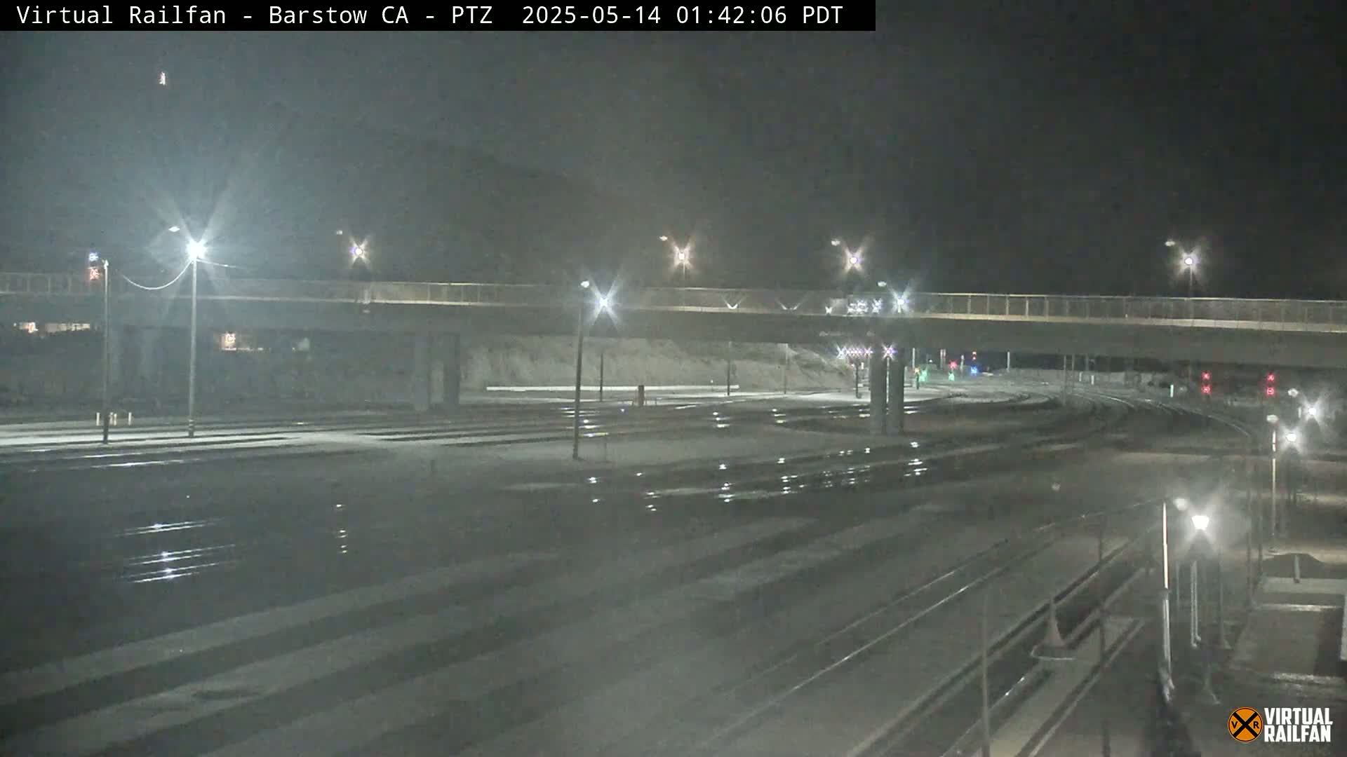 A nighttime view of a snow-dusted railway crossing under a bridge, illuminated by streetlights.