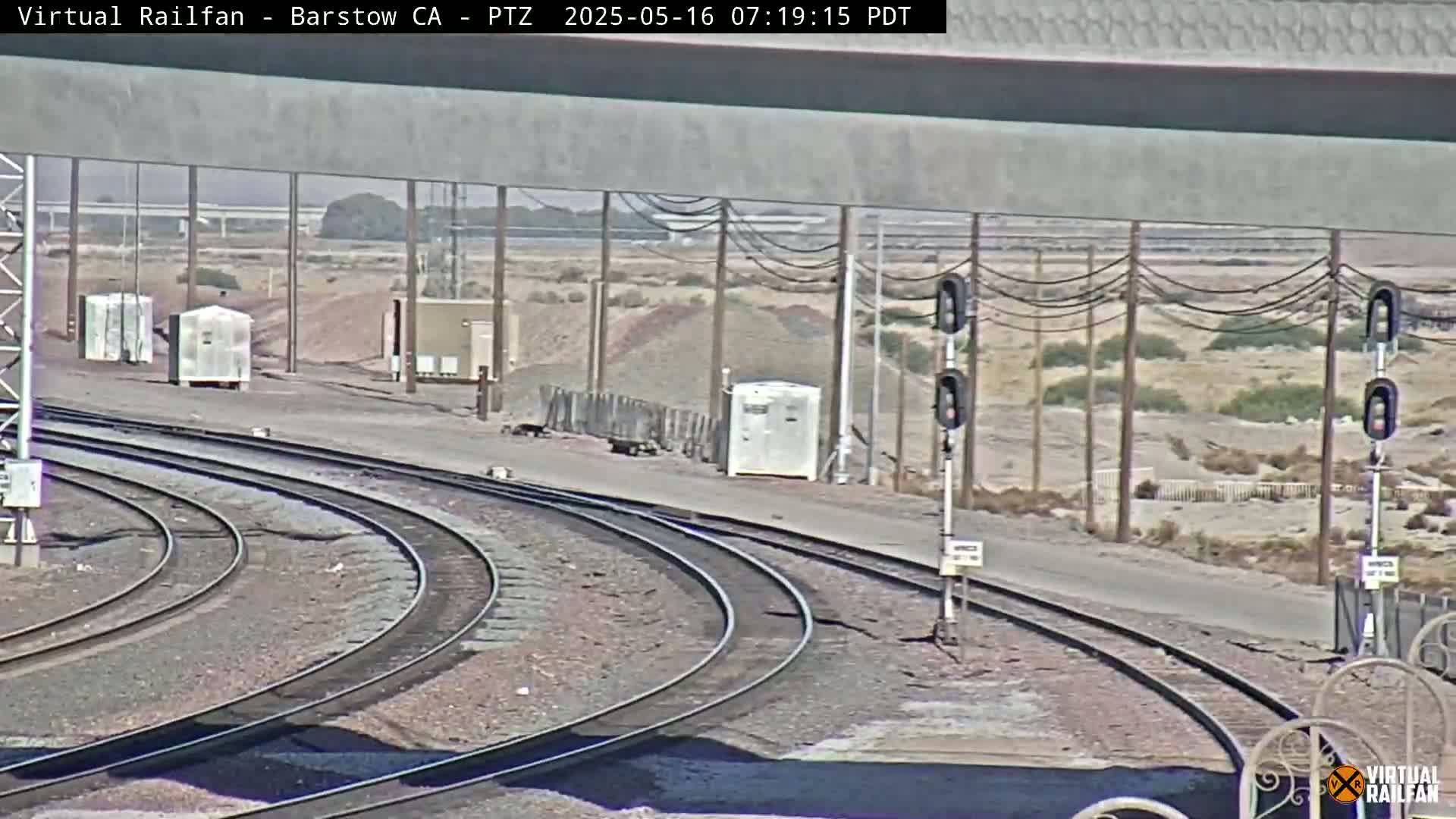 A sunny view of railway tracks curving to the right, with several small buildings and utility poles in the background.