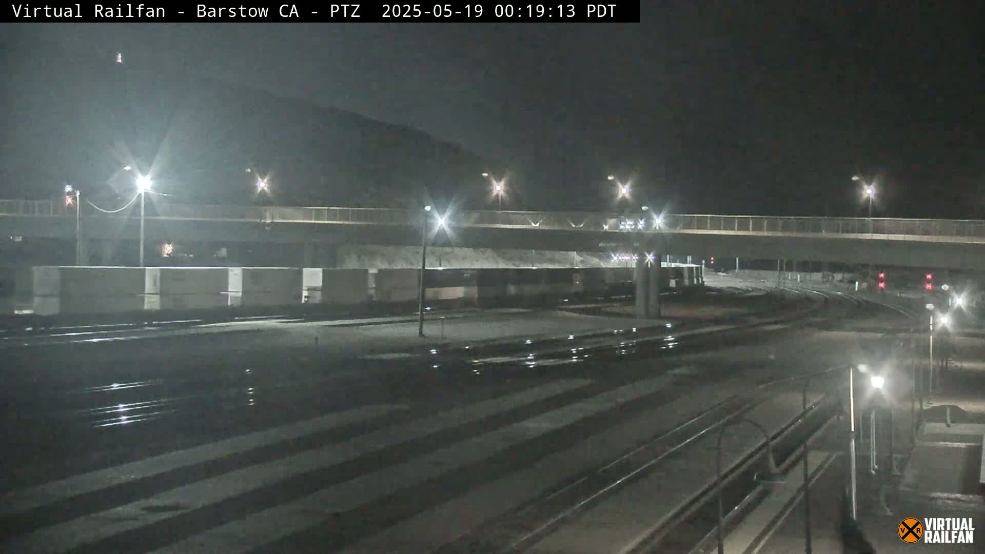 A nighttime view of railroad tracks and a highway overpass under artificial light.