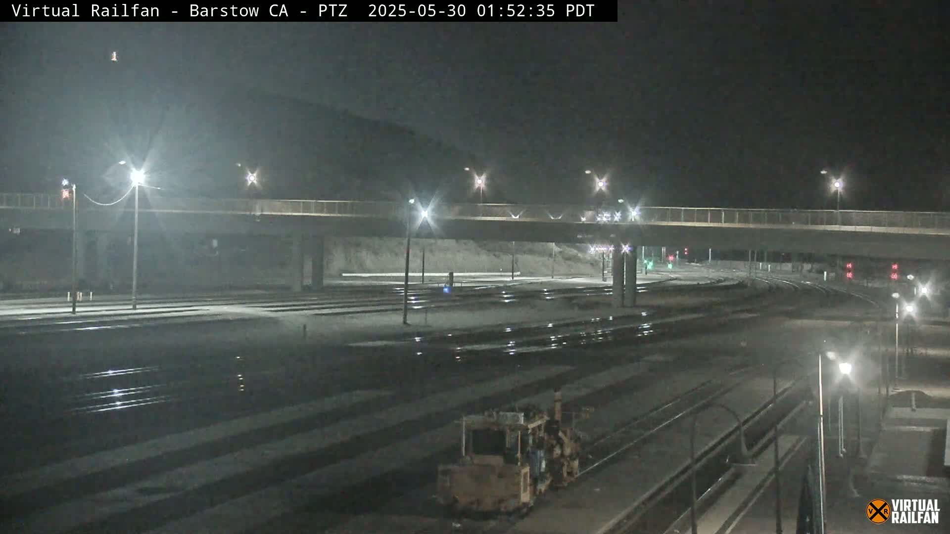 A nighttime view of a rail yard with a road overpass, illuminated by streetlights.