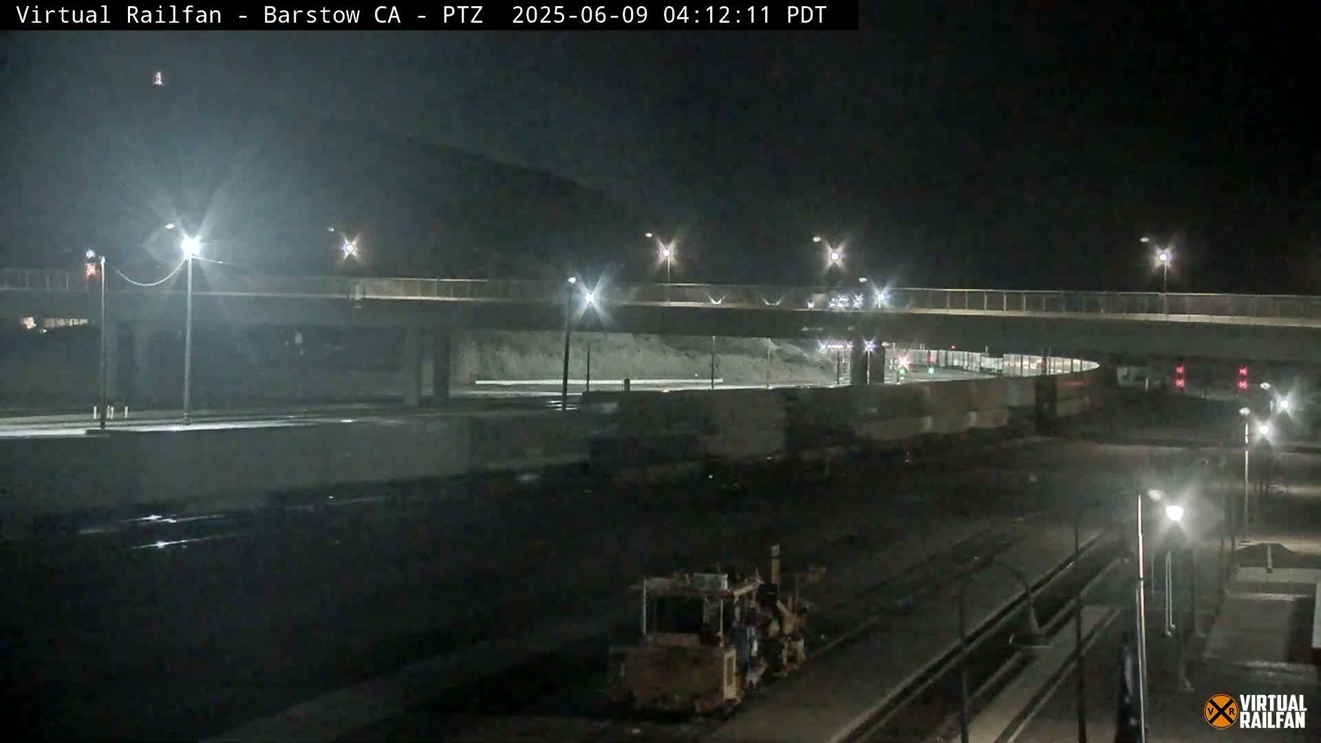 A nighttime view of a rail yard with a road overpass, illuminated by streetlights.