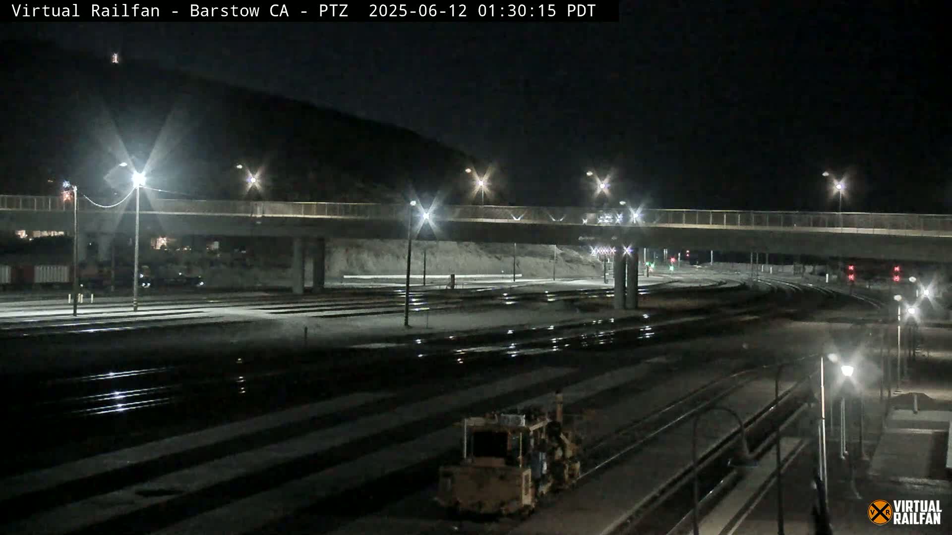 A nighttime view of a railway yard with a road overpass, illuminated by streetlights.