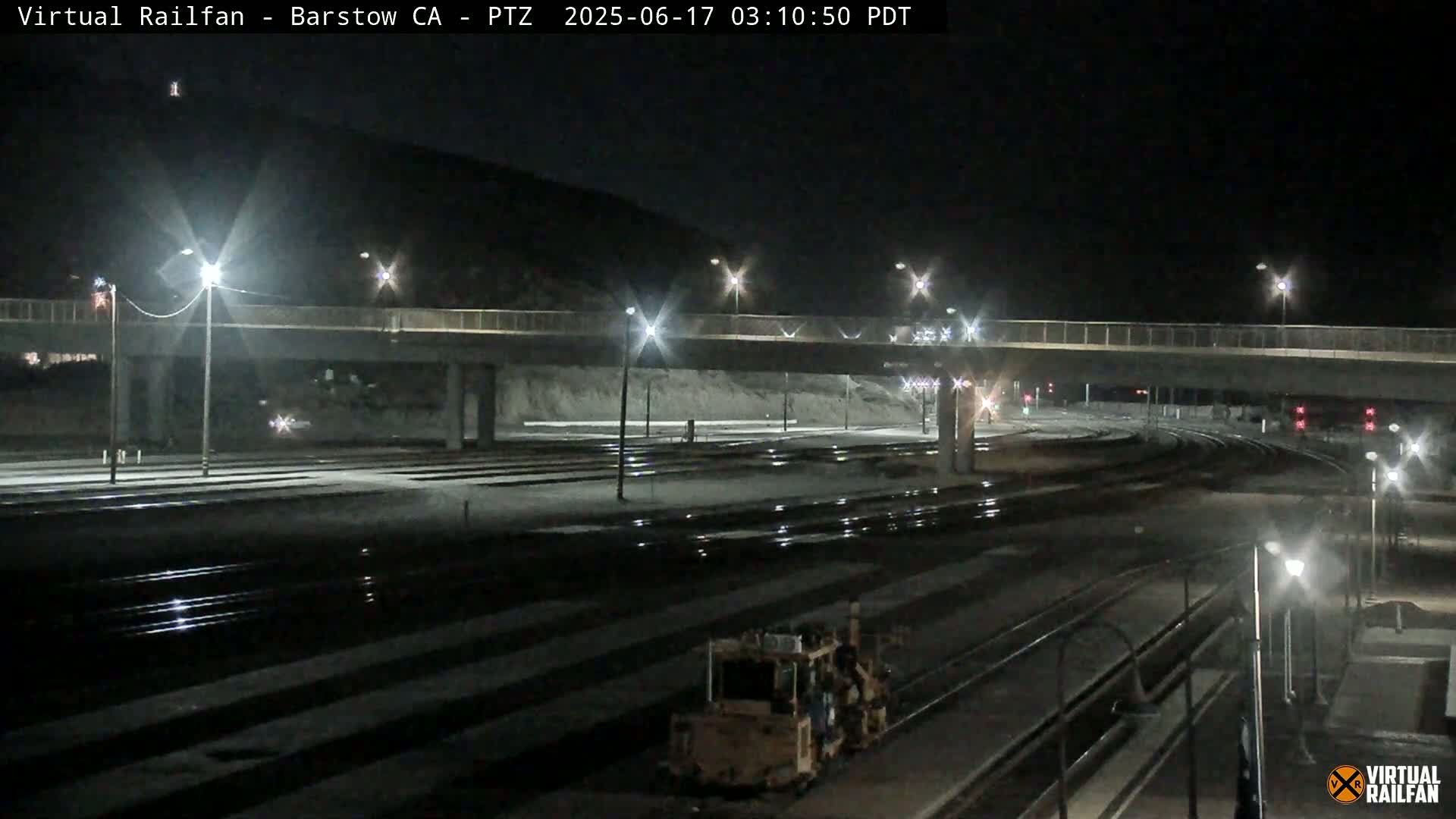 A nighttime view of a rail yard with a roadway overpass, illuminated by streetlights.