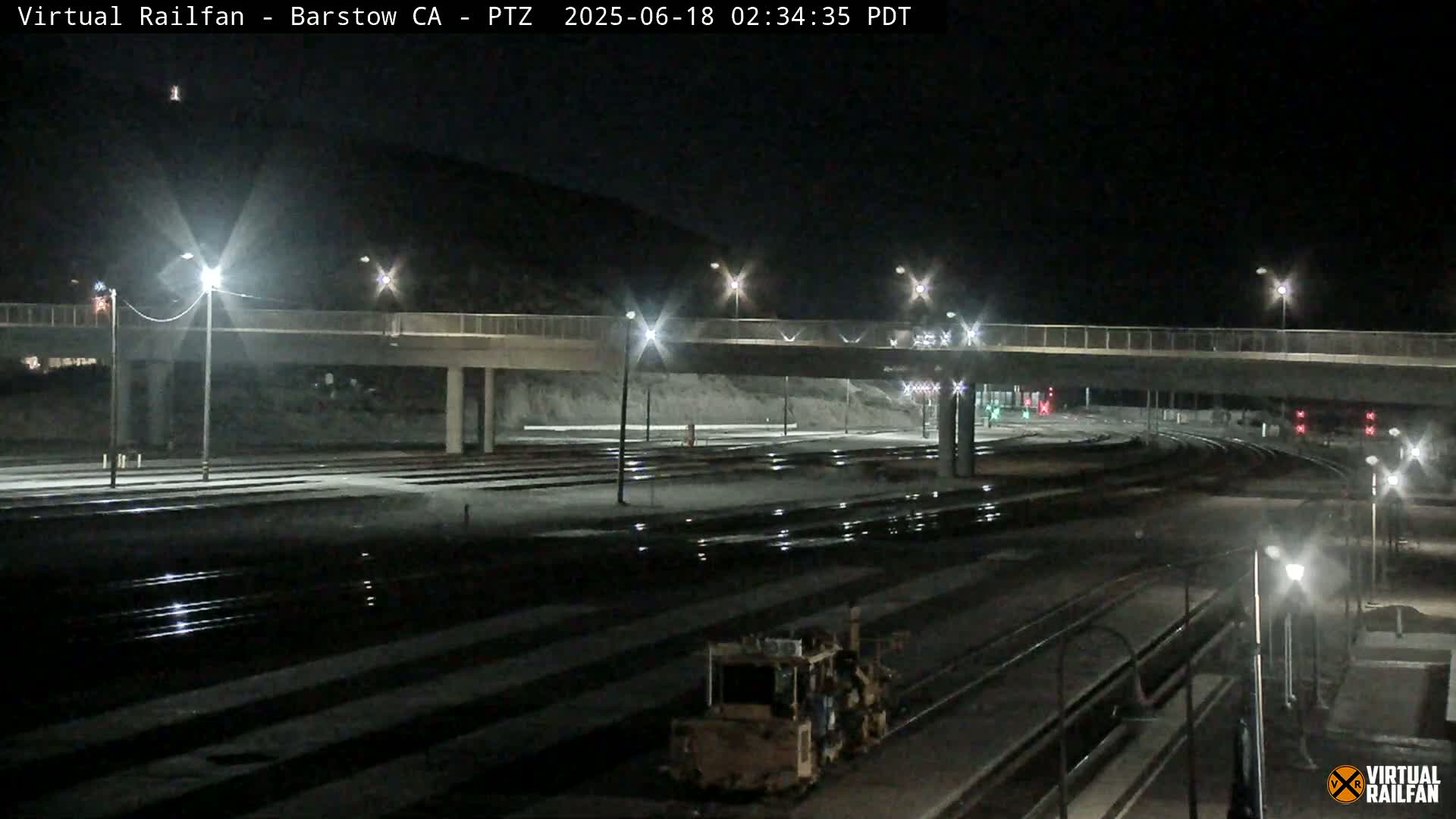 A nighttime view of a rail yard with a road overpass, illuminated by streetlights.