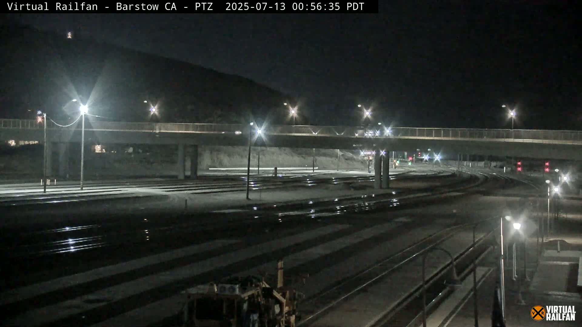 A nighttime view of a rail yard with a roadway overpass, illuminated by streetlights.