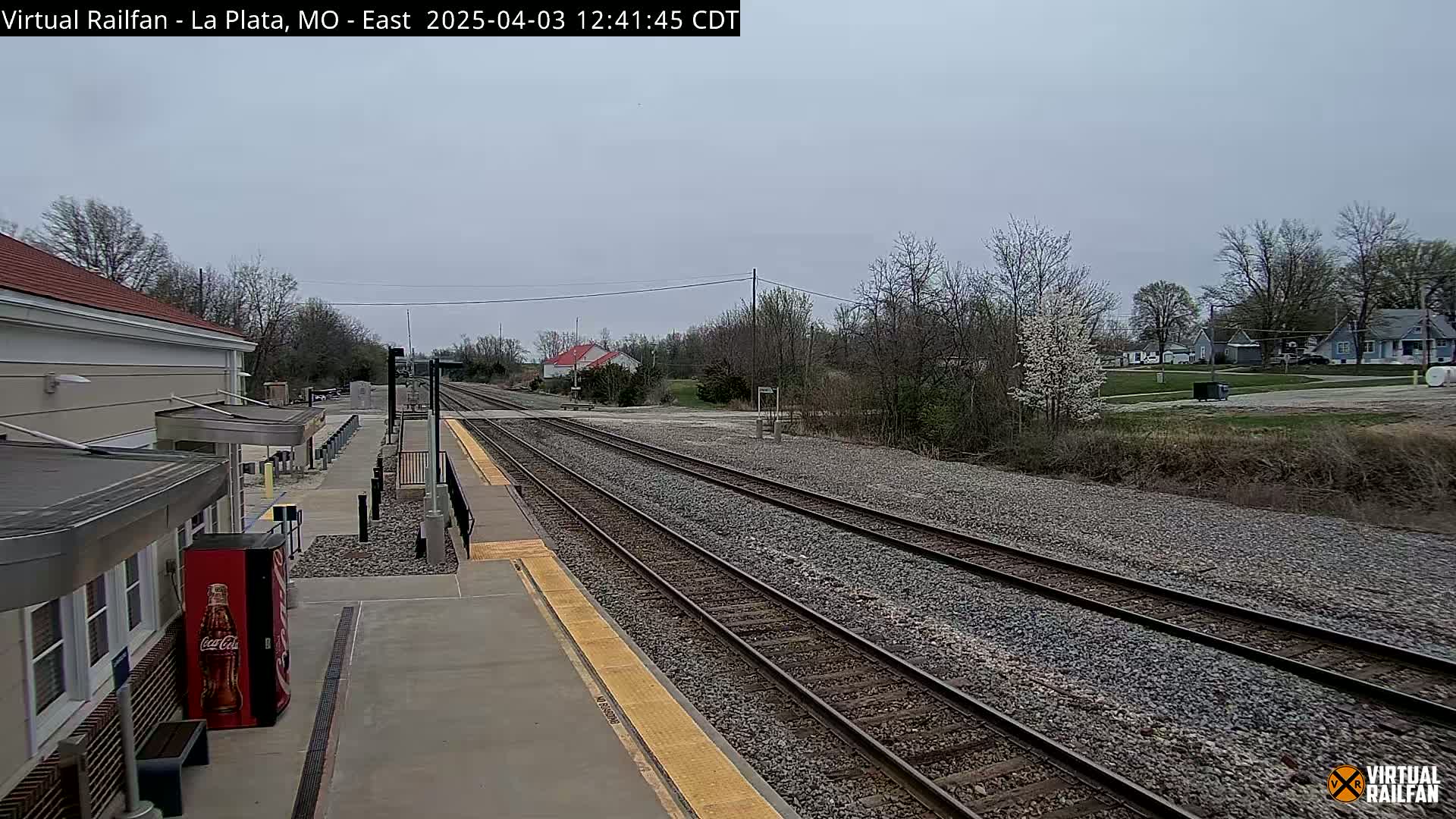 A train station platform with multiple train tracks extending into a residential area under an overcast sky.