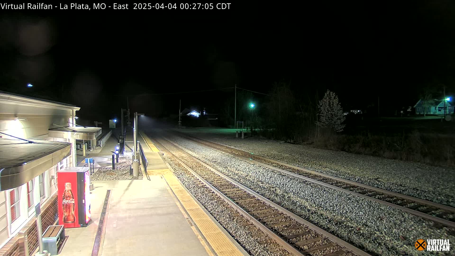 A nighttime view of a deserted train station platform with two sets of train tracks extending into the darkness.