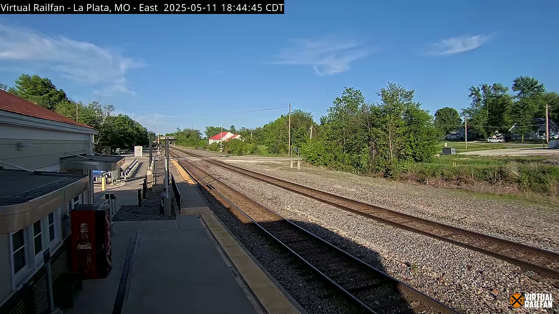 A train station platform with two sets of train tracks extending into the distance under a mostly sunny sky.