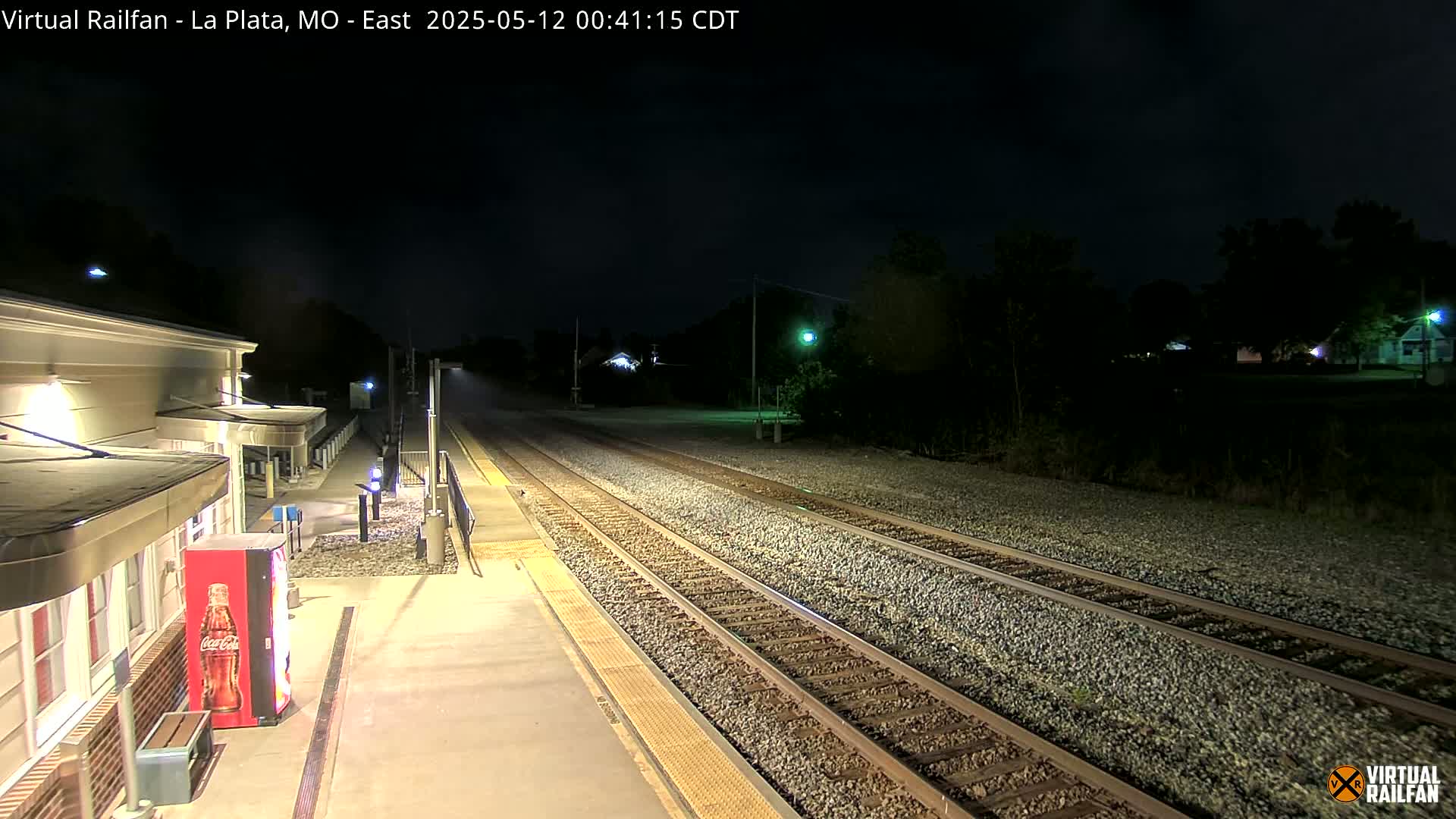 A nighttime view of a train station platform with train tracks extending into the darkness.