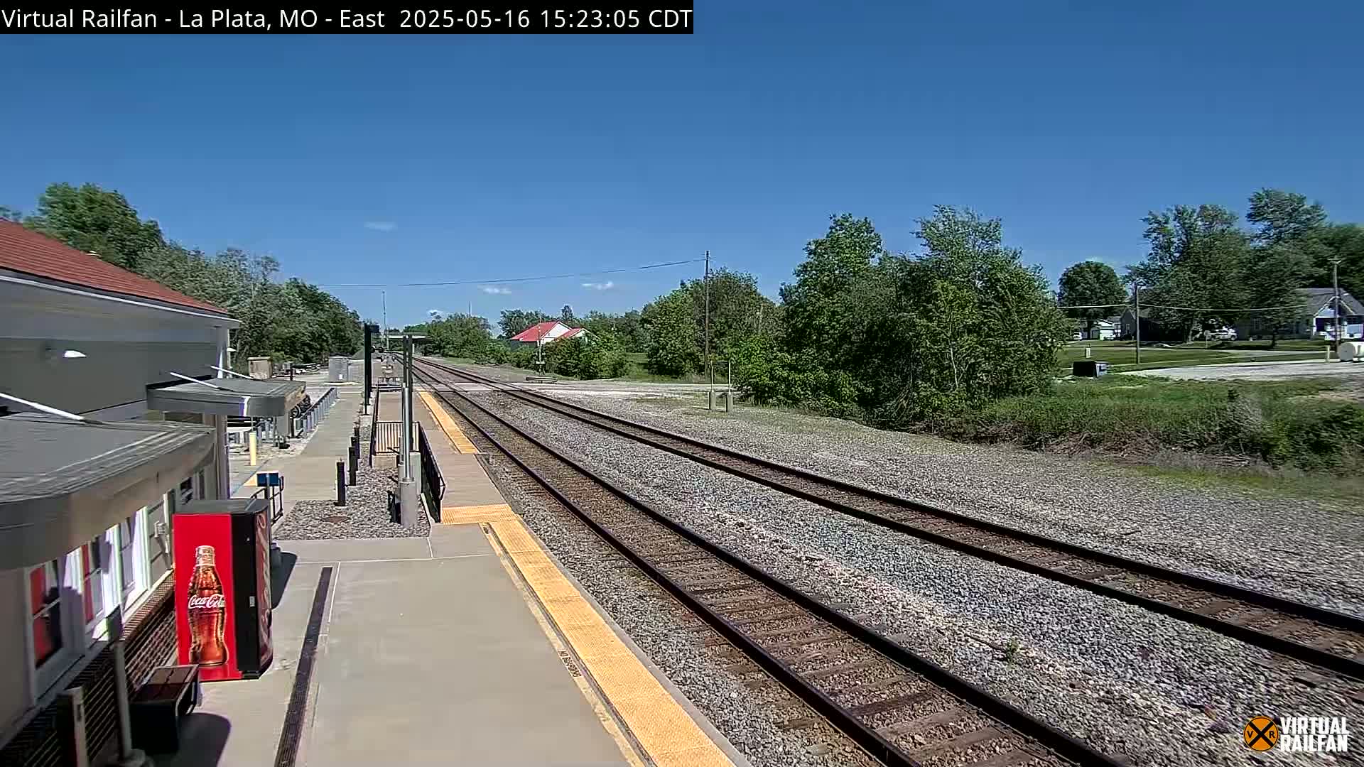 A train station platform with two sets of train tracks extending into the distance under a clear blue sky.