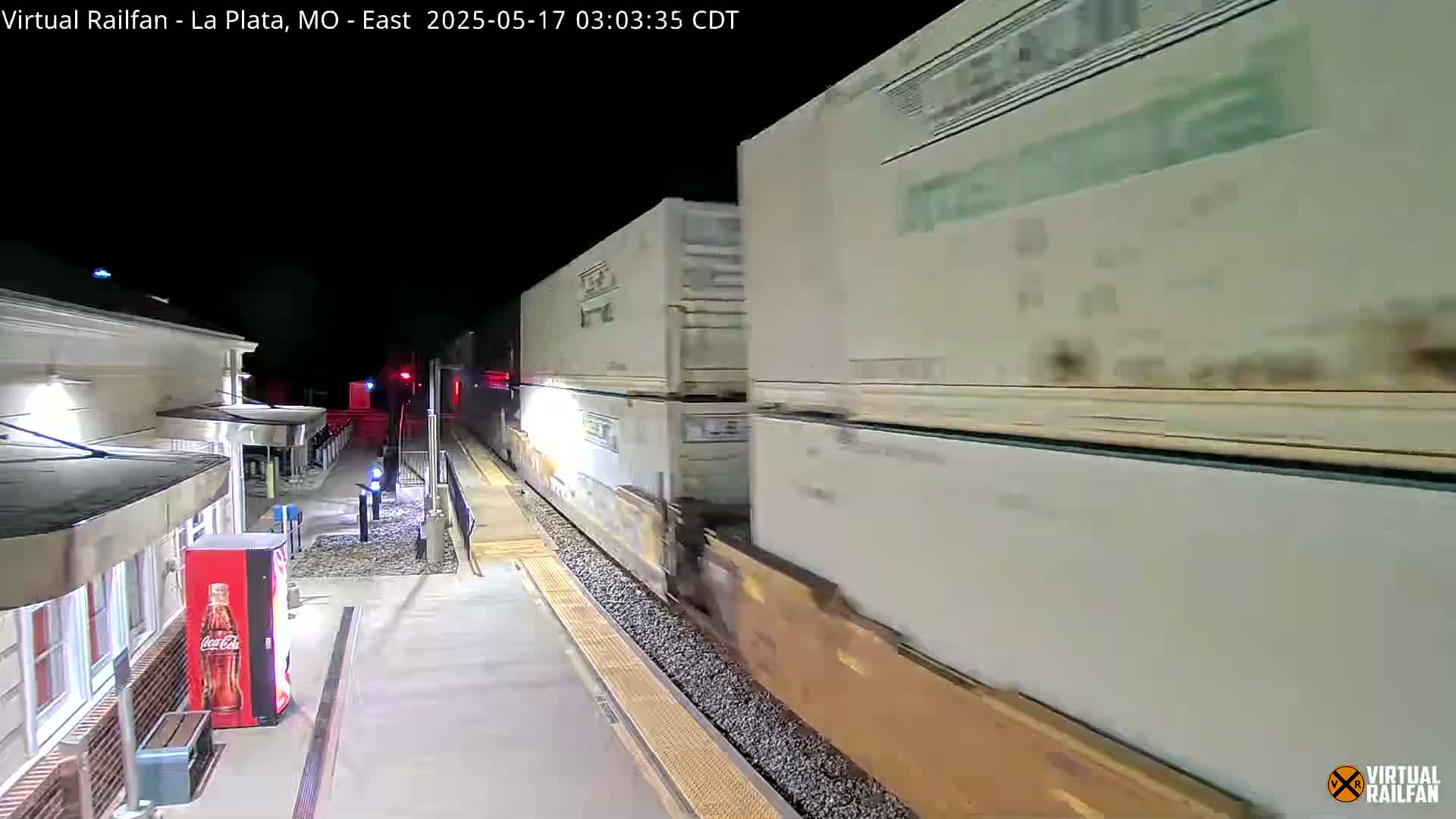 A long freight train passes by a station at night.