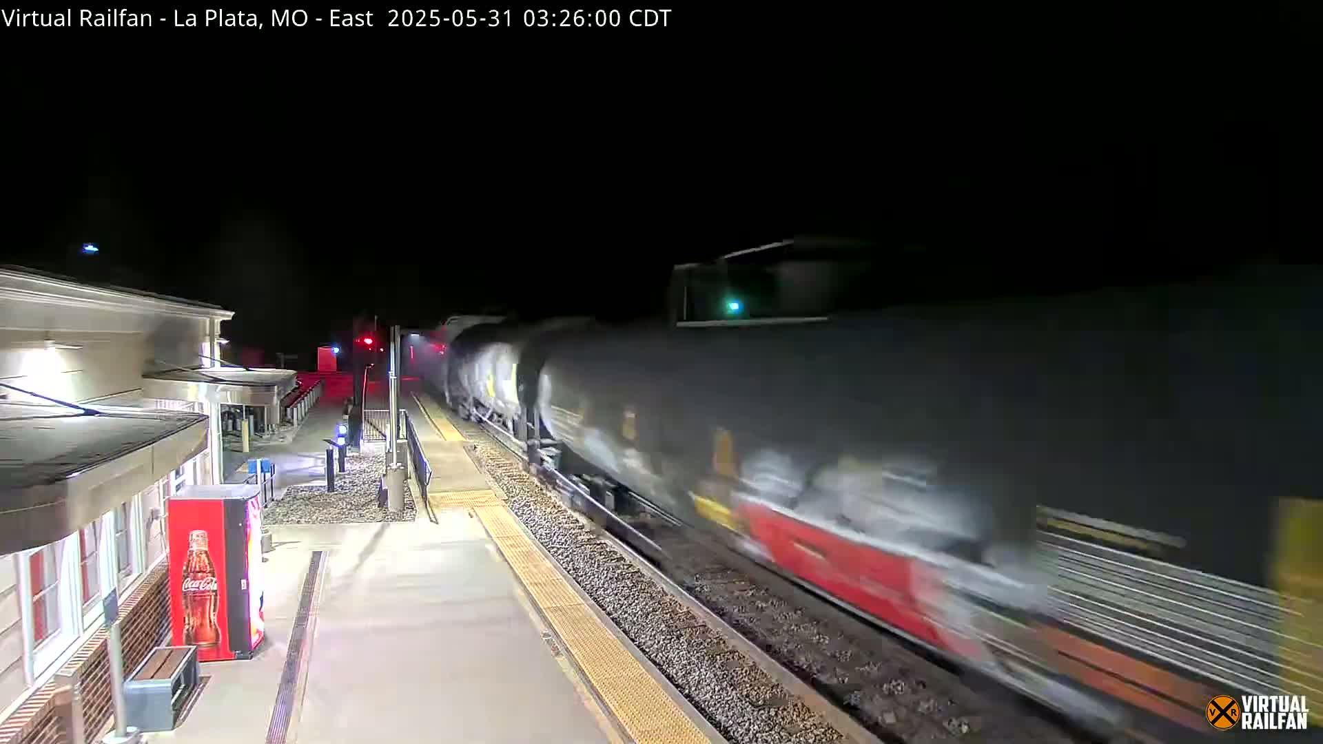 A long freight train passes a train station at night.