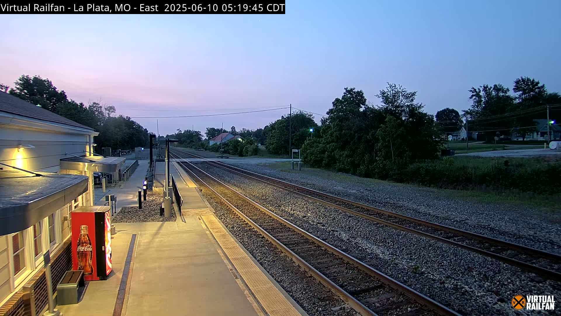 A train station platform at twilight, with multiple train tracks extending into the distance past a small town.