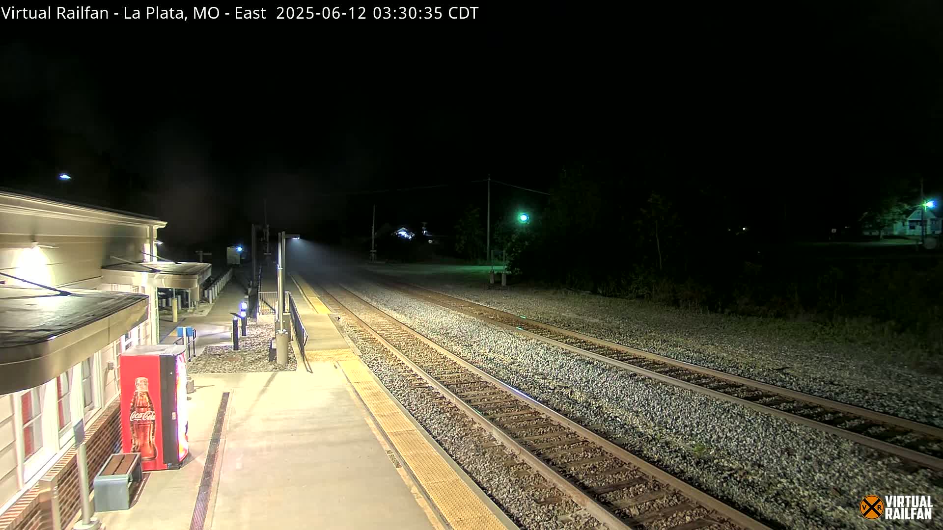 At night, a mostly empty train station platform and a set of train tracks extend into the darkness.