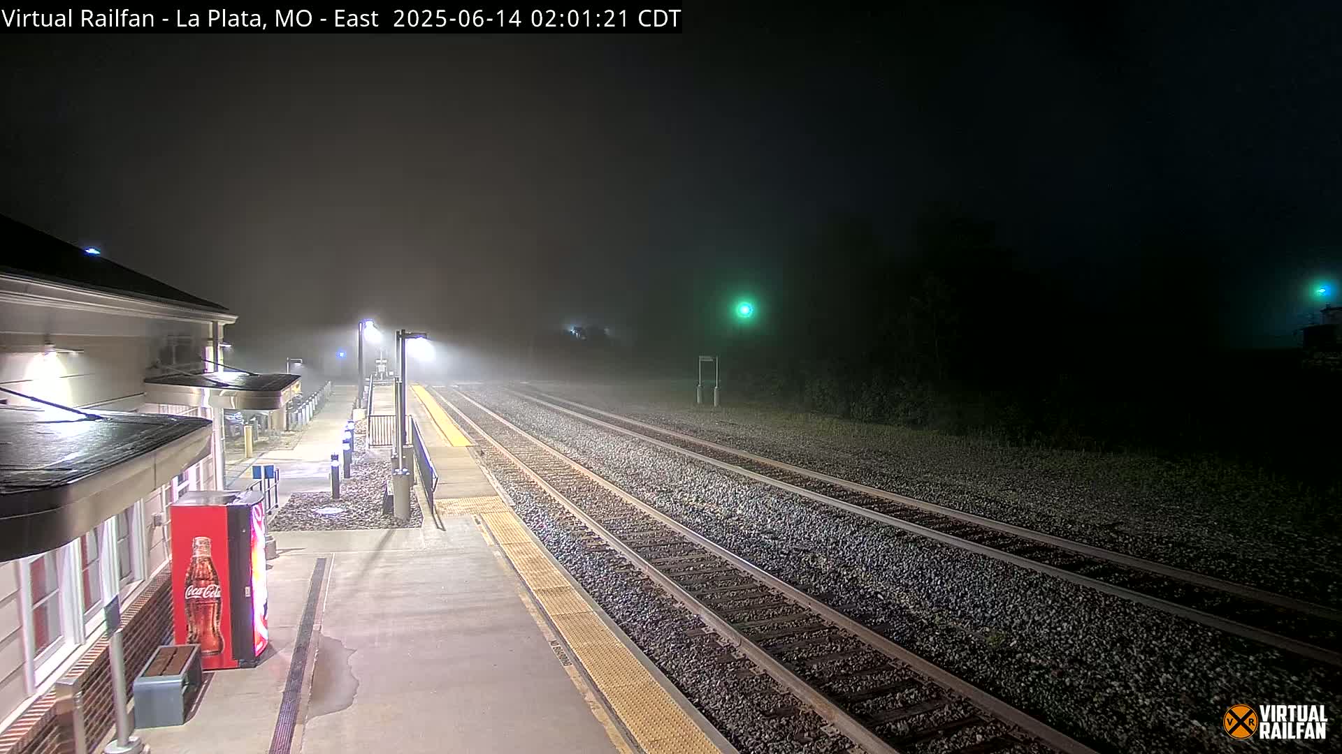 A nighttime, foggy view of a train station platform with several tracks extending into the distance.