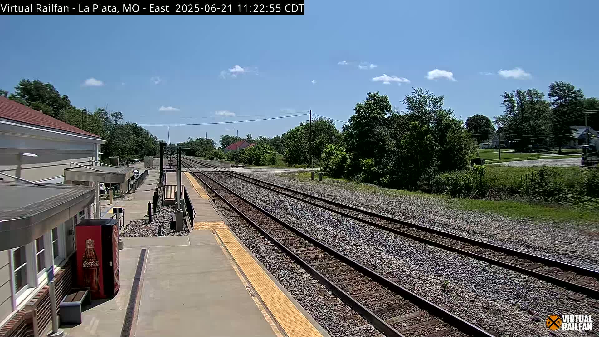 A train station platform with several tracks stretches into the distance under a partly sunny sky.