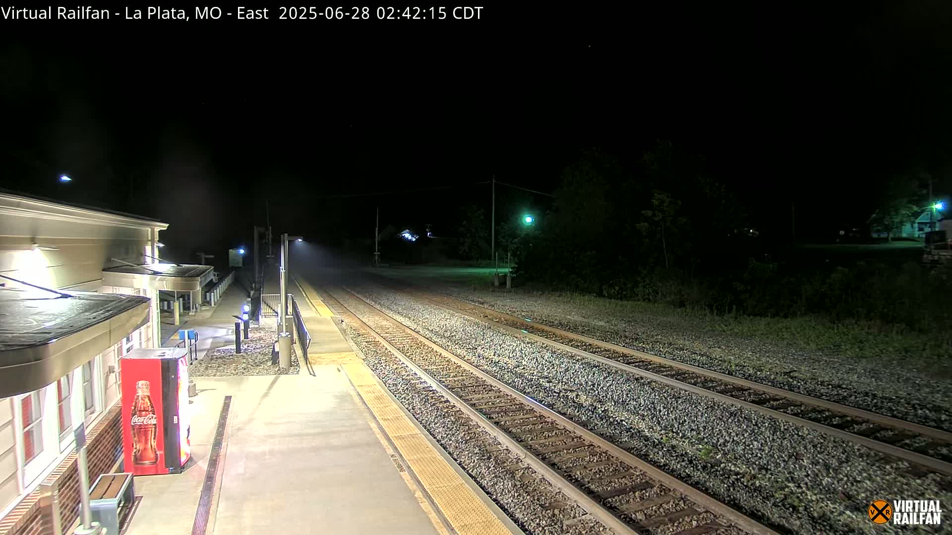 A nighttime view of a train station platform with train tracks extending into the darkness, under clear skies.