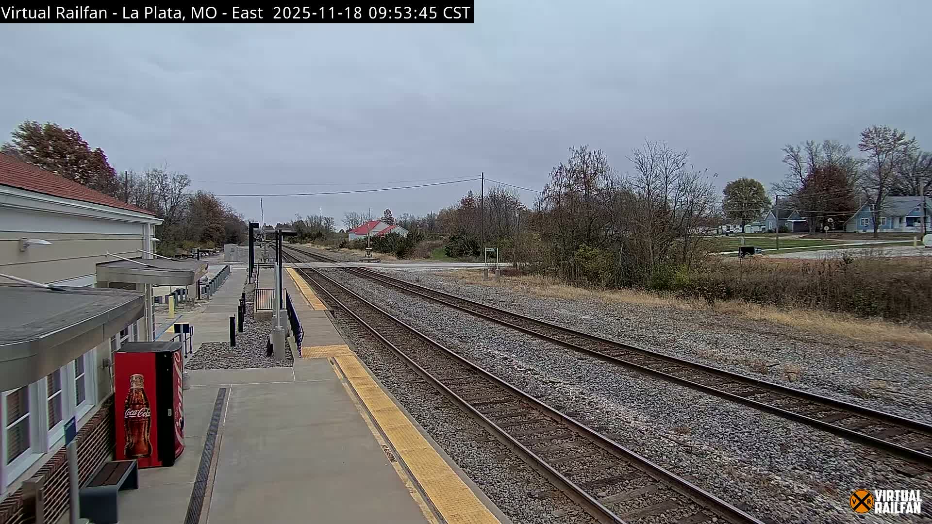 A nighttime view of a train station platform and tracks, with a light mist or fog in the air.