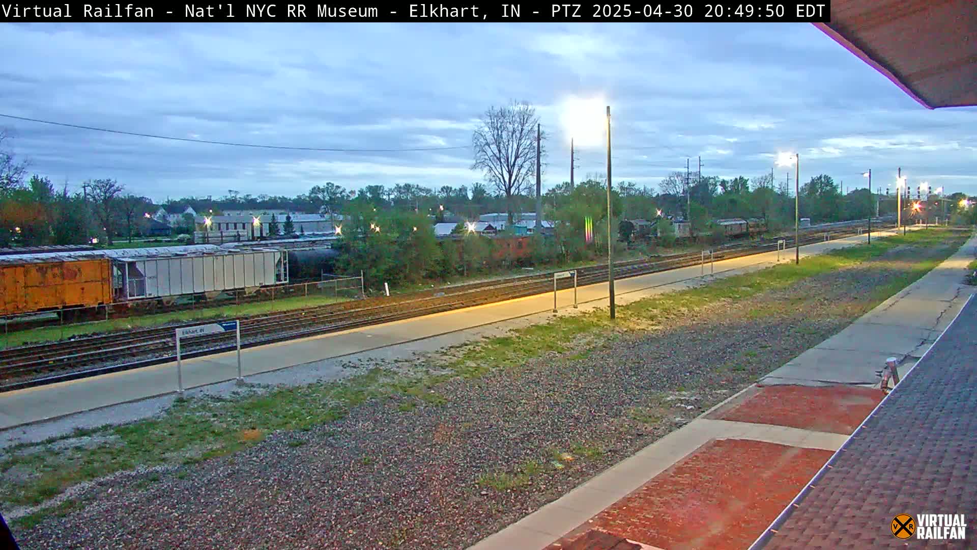 A twilight view of railroad tracks and several freight cars, with sparse vegetation along the sides.