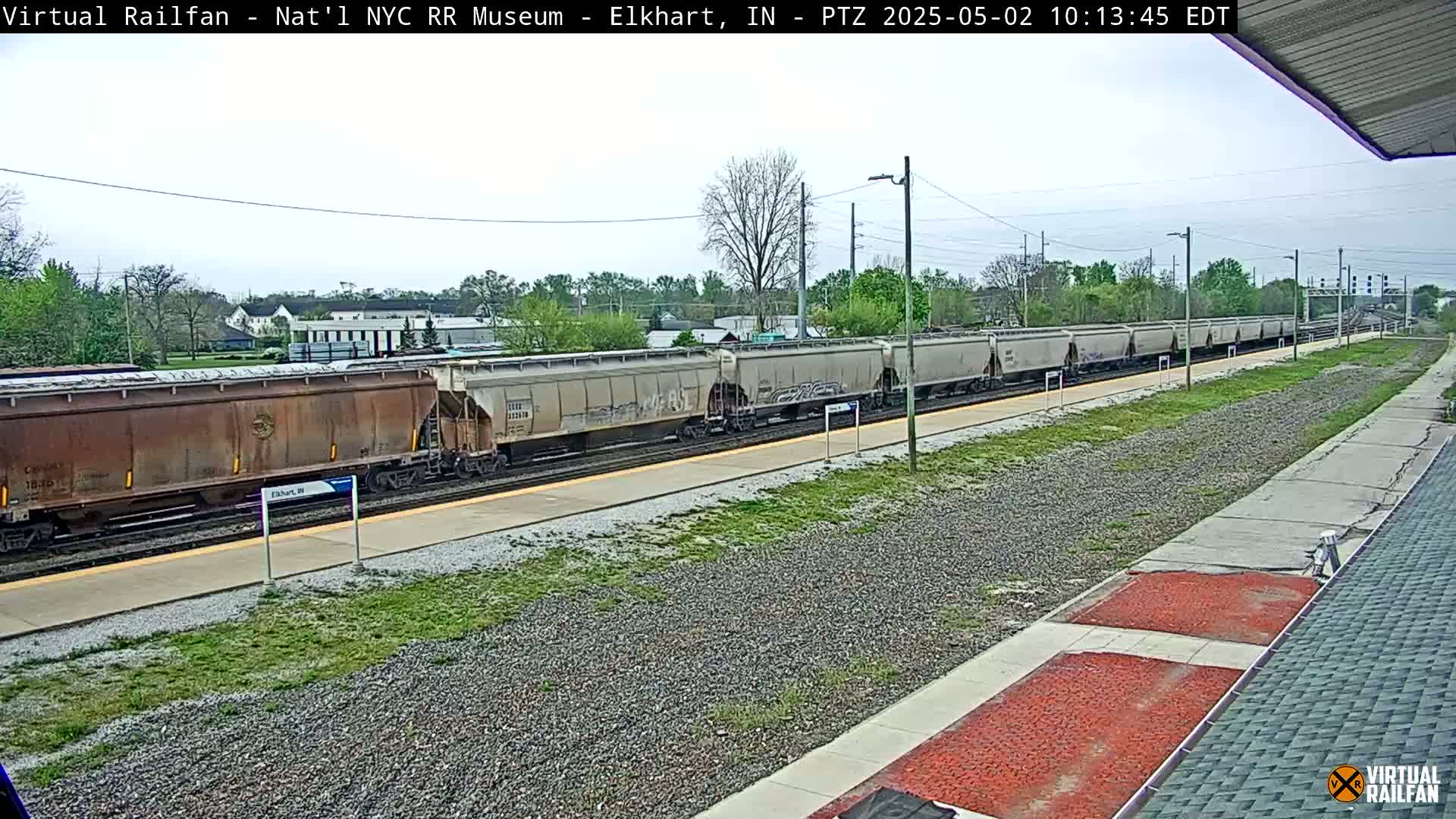 A long freight train sits at a station on a partly cloudy day.