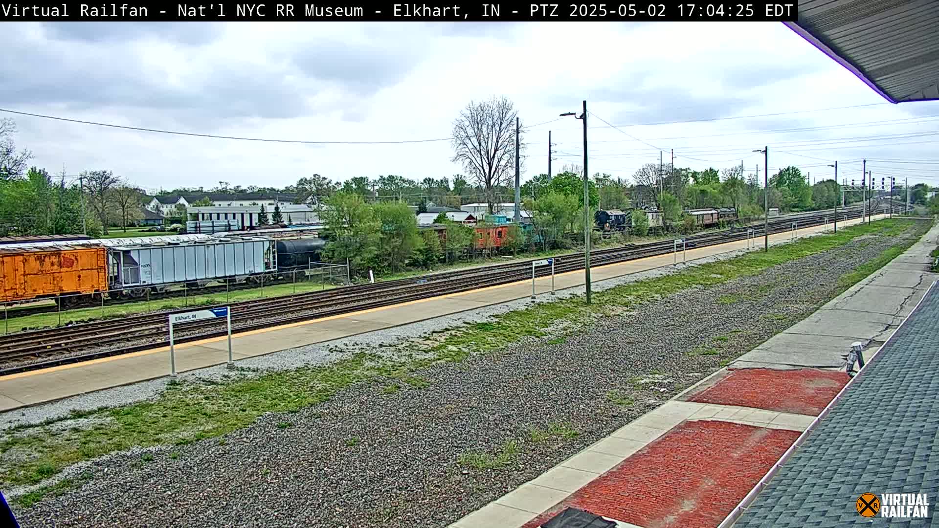 A mostly sunny day shows a train station with several train cars and a platform.