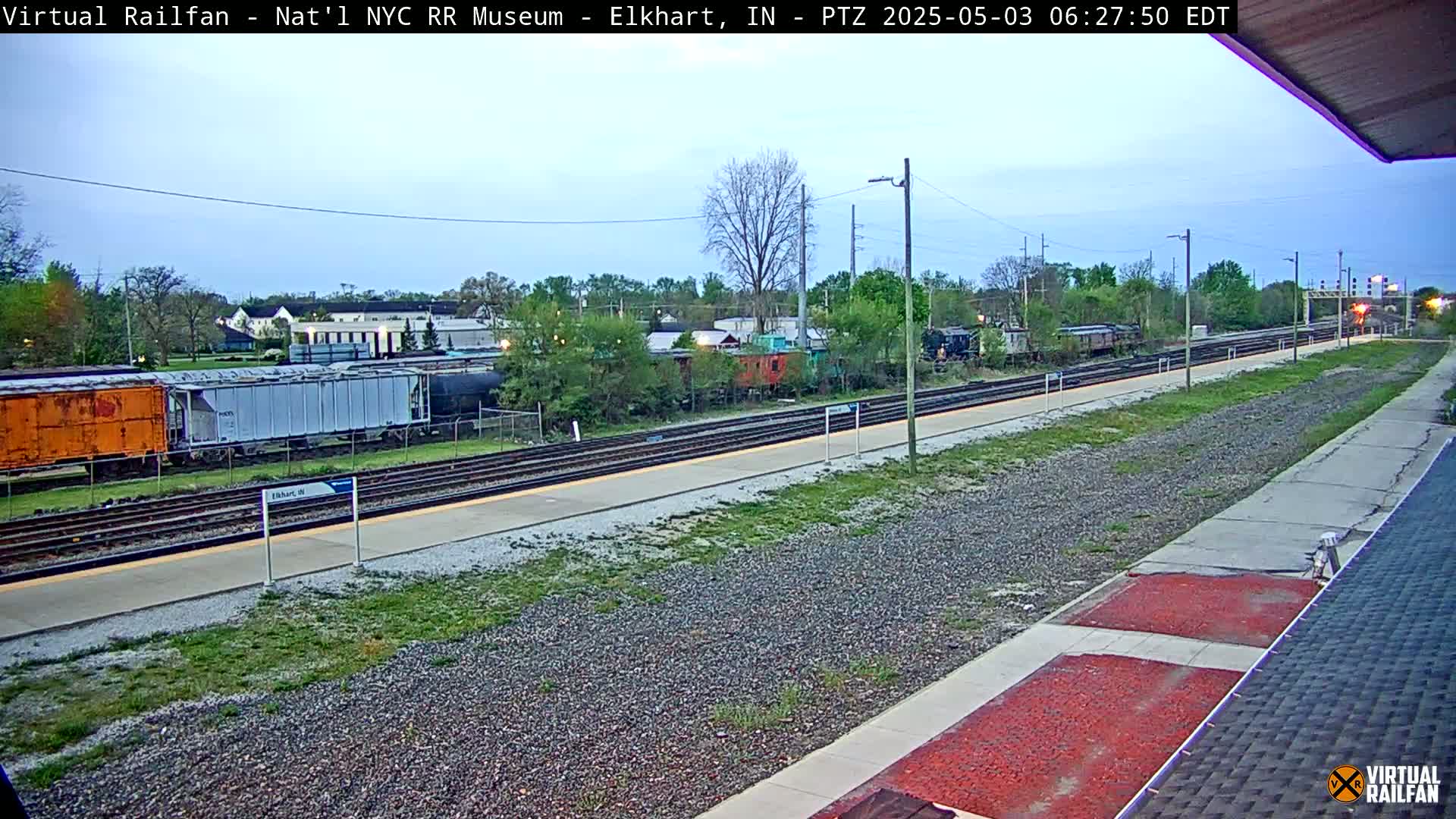 A train station platform with several freight cars and a train in the background, under a twilight sky.