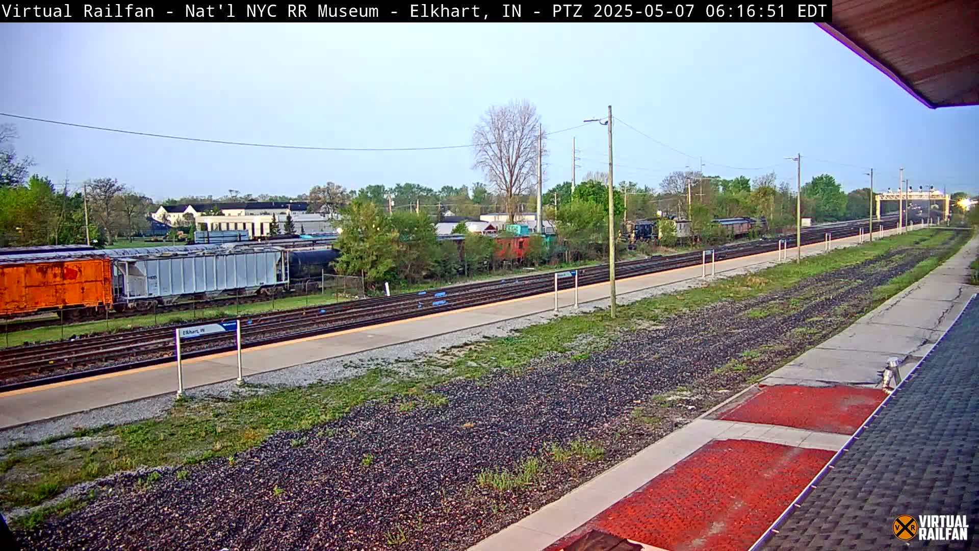 A mostly clear daytime view of a train station with several freight cars on the tracks and a platform extending into the distance.