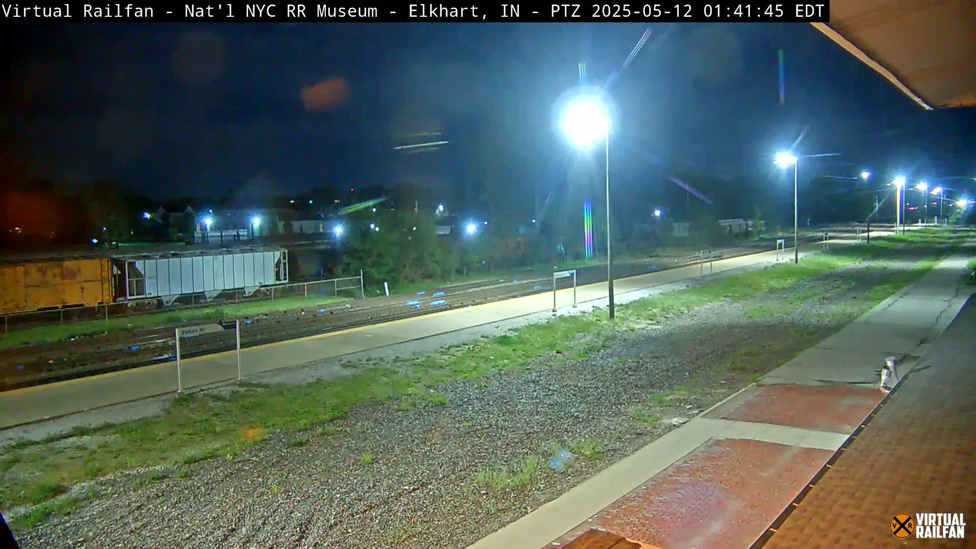 A nighttime view of a train platform with several railway cars, illuminated by bright streetlights.