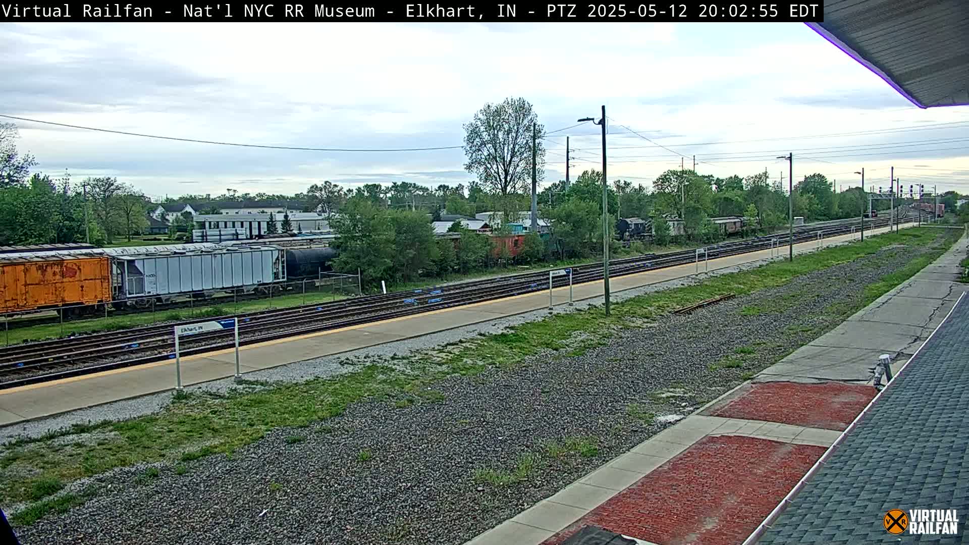 A train station platform with several freight cars and a partially cloudy sky.