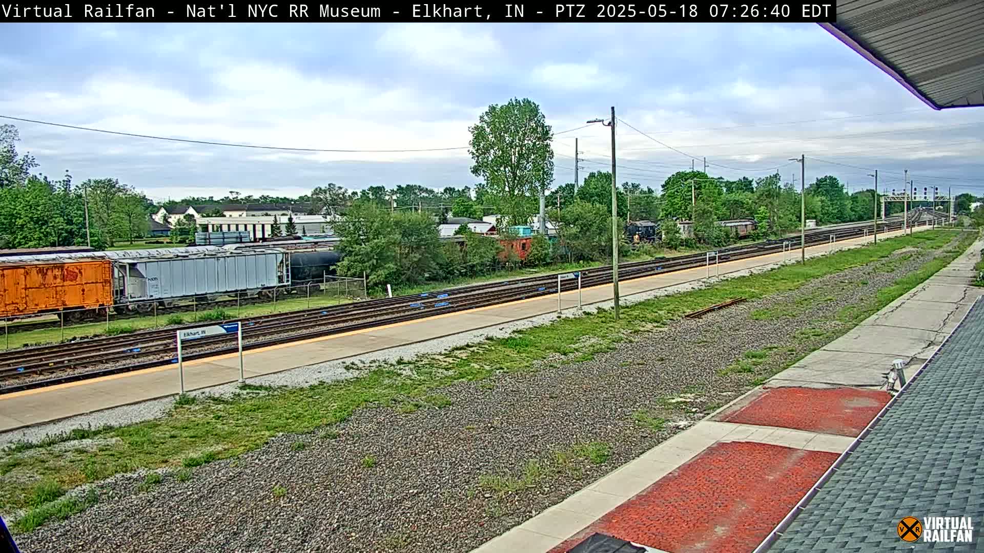 A train station with several rail cars and tracks visible under a partly cloudy sky.