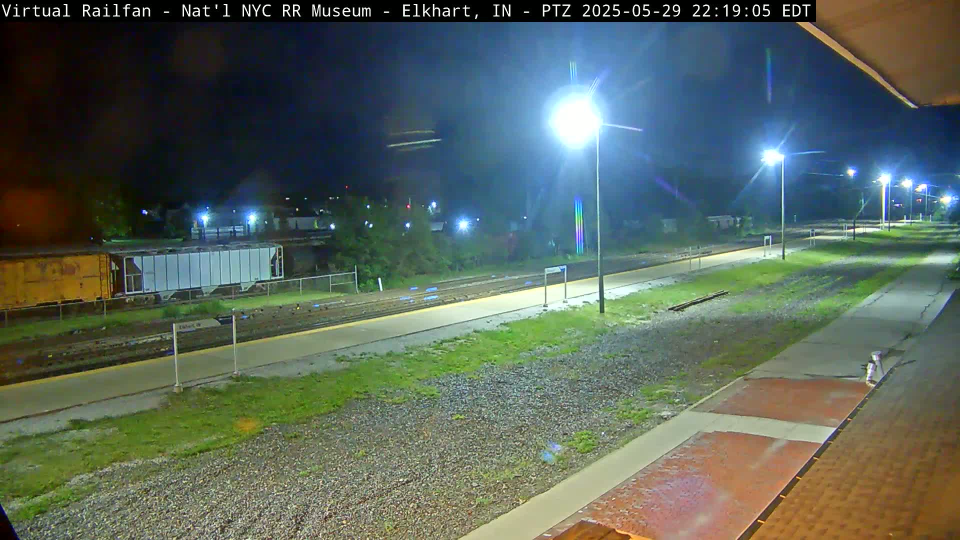 A nighttime view of a train platform with rail lines, several parked railcars, and bright lights illuminating the scene.