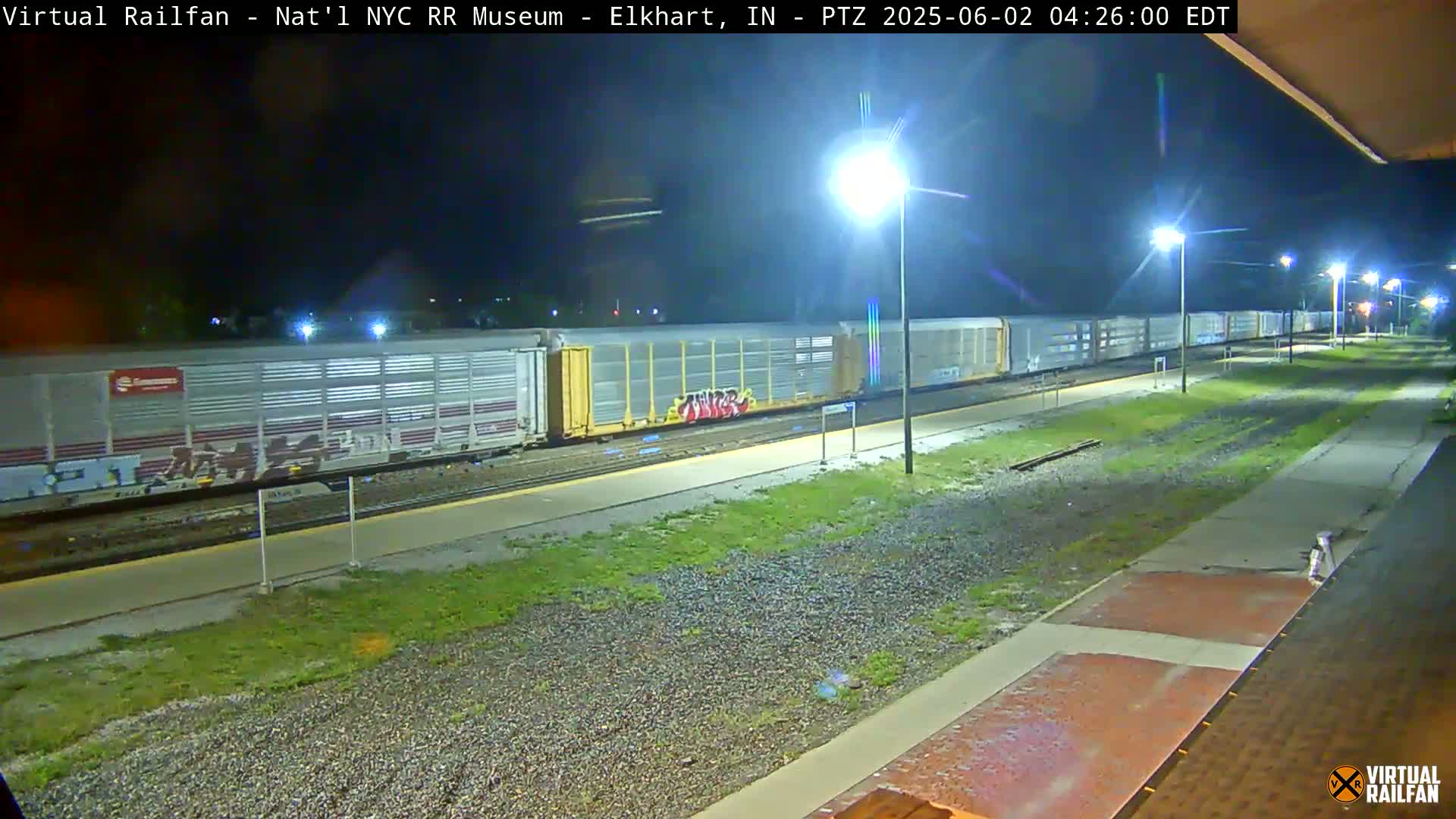 A long freight train sits at night in a rail yard illuminated by several streetlights.