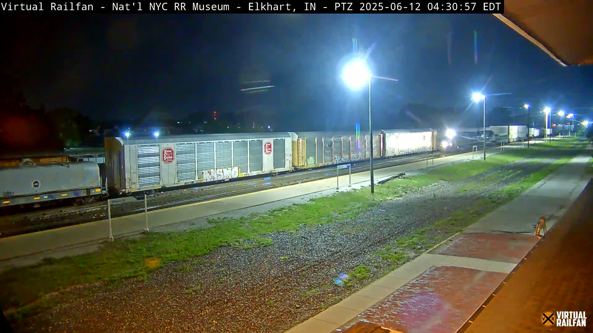 A nighttime view of a freight train alongside a platform, illuminated by streetlights.