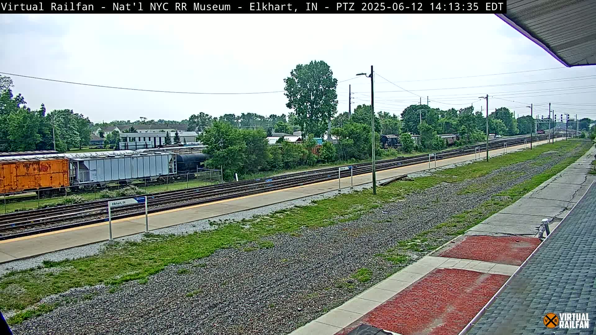 A train station platform with several rail lines and freight cars under a partly cloudy sky.