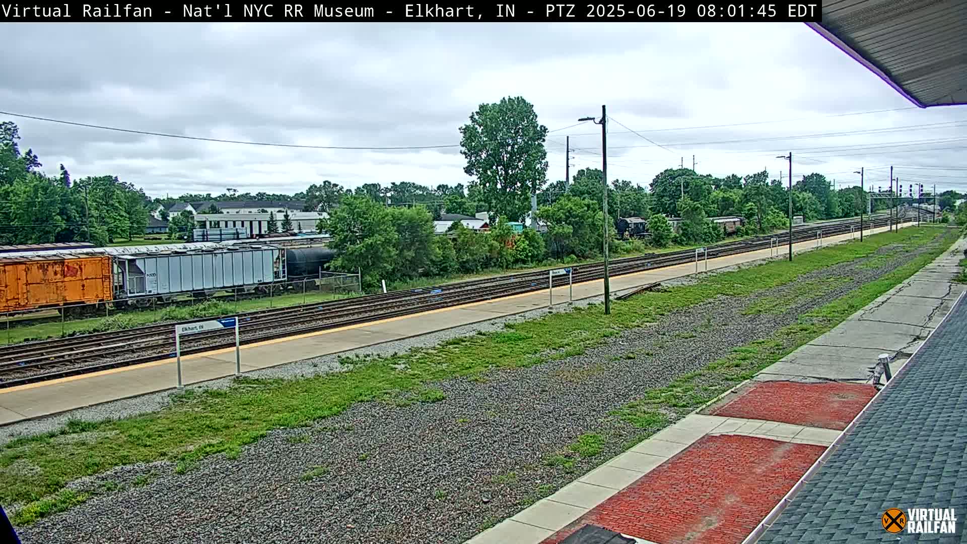 A mostly cloudy day at a train station shows multiple railway tracks, several freight cars, and a grassy area.